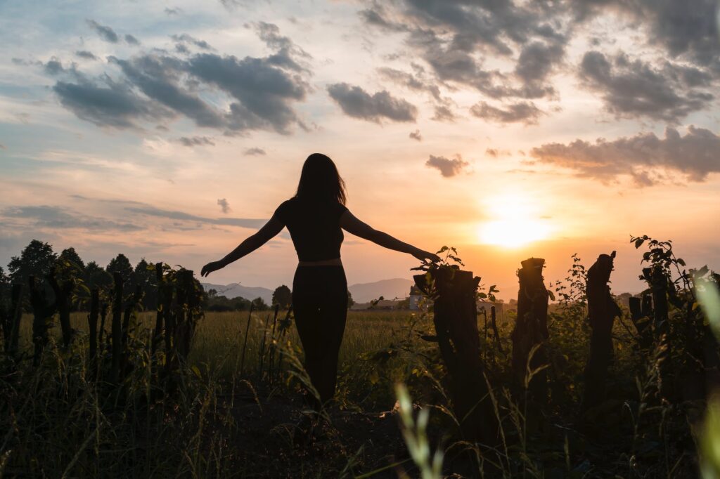 back view of a woman standing on grass field during sunset