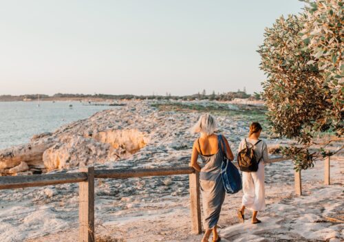 two women are walking away from sandy beach at sunset