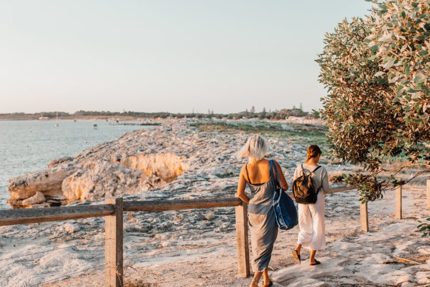 two women are walking away from sandy beach at sunset