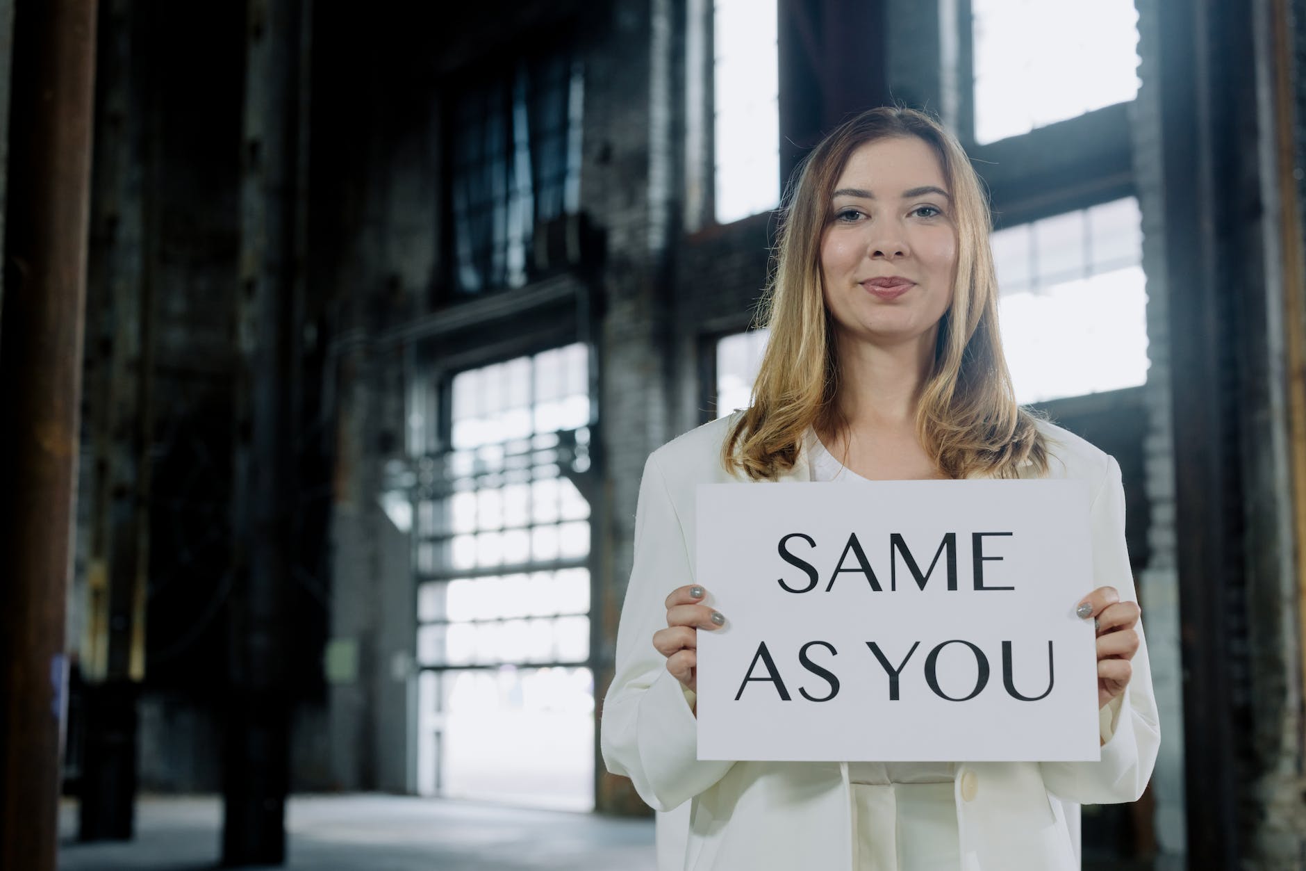 a woman in white blazer holding white paperboard with a text same as you