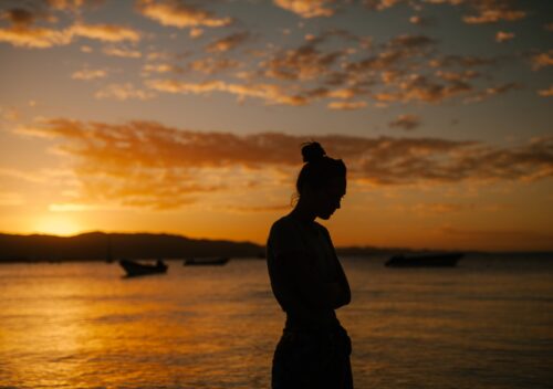 sad woman standing on coast of sea at sunset