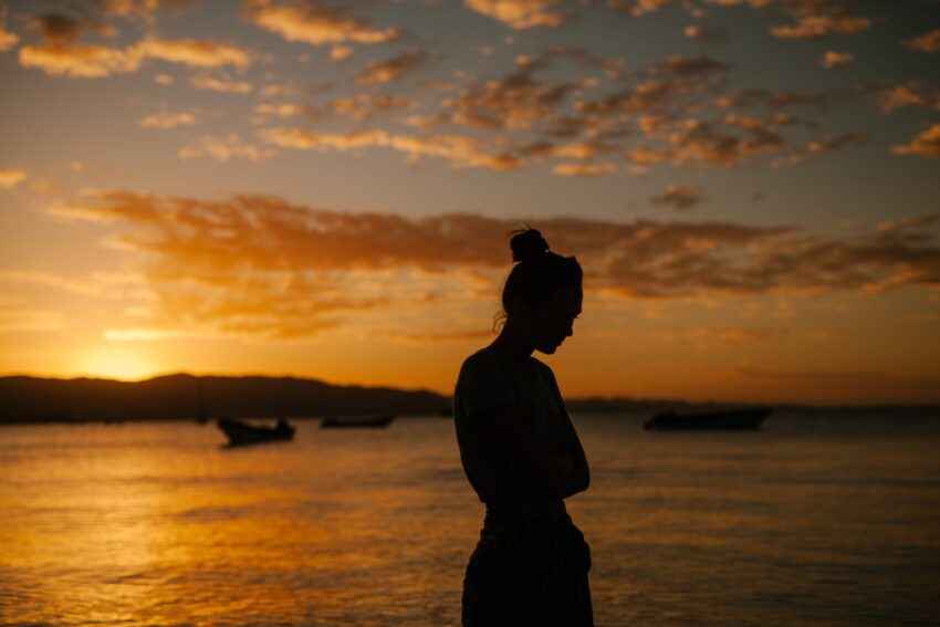 sad woman standing on coast of sea at sunset