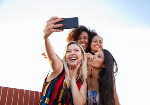 cheerful multiethnic girlfriends taking selfie on smartphone on sunny day