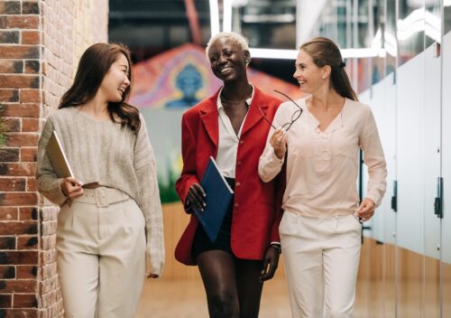 diverse successful businesswomen smiling and walking together in modern workplace